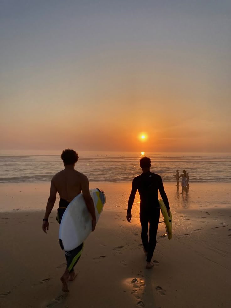 Surferja se vračata s plaže ob sončnem zahodu